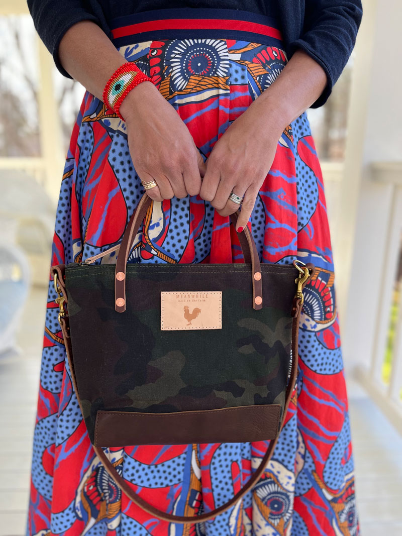 A woman wearing the camouflage bag with dark brown straps and the meanwhile logo.