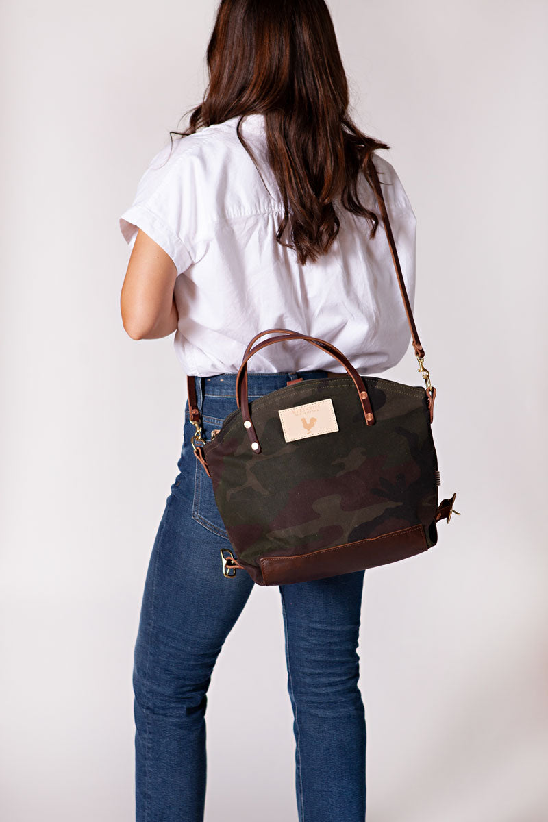 A woman wearing the camouflage backpack with dark brown straps and the meanwhile logo.