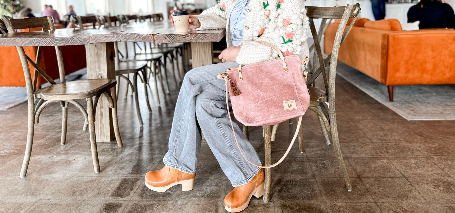 Girl sitting at table holding small rose pink leather handbag