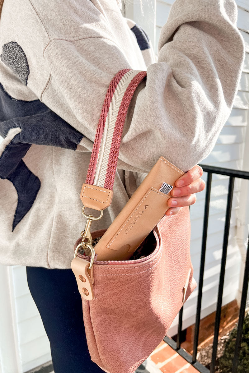 Girl putting a small beige wallet into the Rose Leather Sling Bag with a Rose Webbing Crossbody Strap