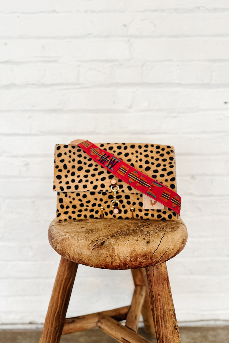 A cheetah print clutch with a personalized Red Aztec Crossbody Strap on a stool