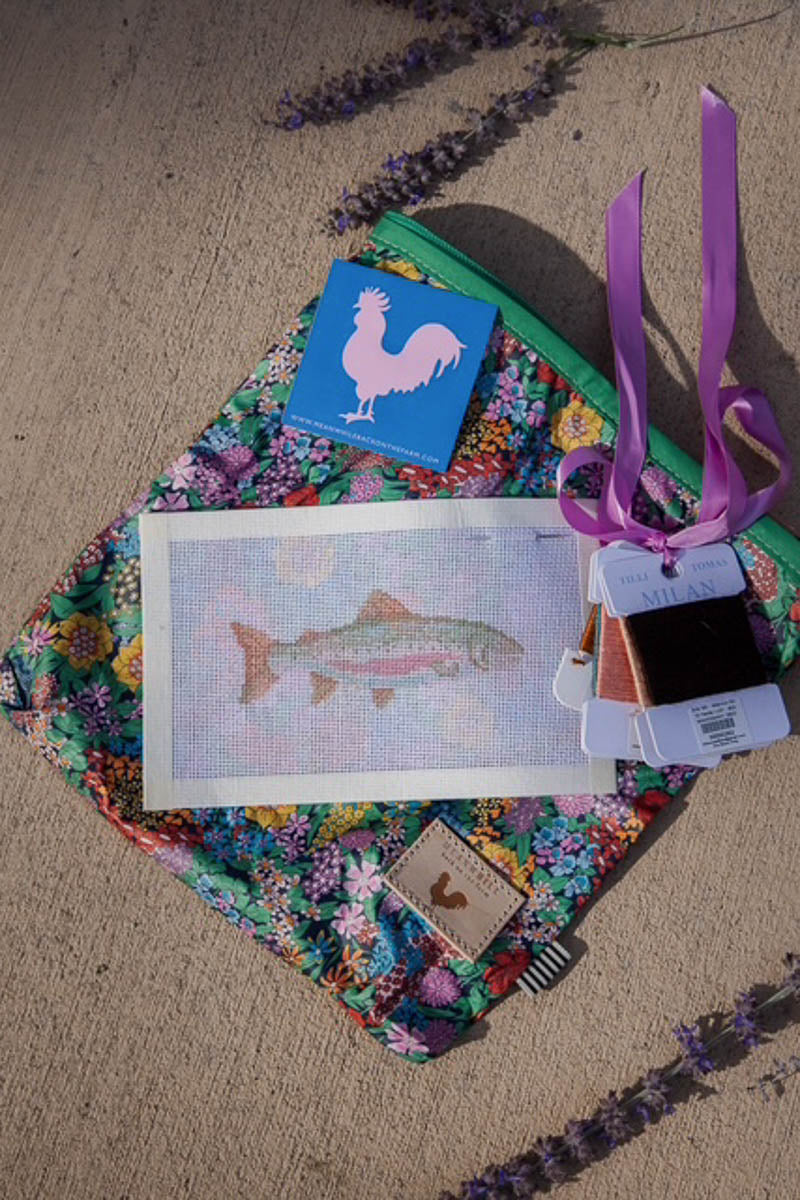 A colorful floral zippered pouch laid on concrete with lavender sprigs around it. On top of the pouch is a framed fish artwork, a blue square with a pink rooster silhouette, ribbon ties, and several fabric swatch tags. Handcrafted by Meanwhile Back on the Farm in Lynchburg, Va.