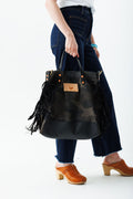Woman holding graphite camouflage wax canvas backpack with fringe