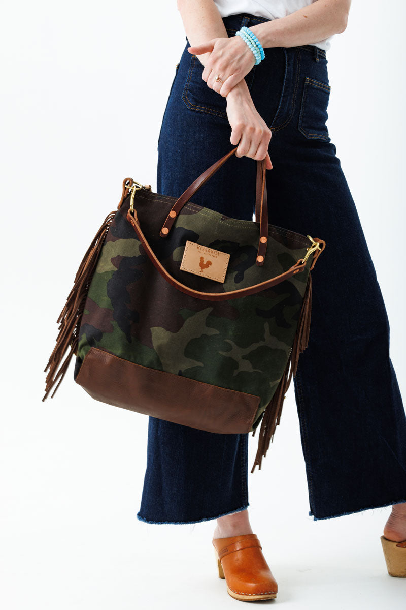 Woman holding camouflage wax canvas backpack with fringe