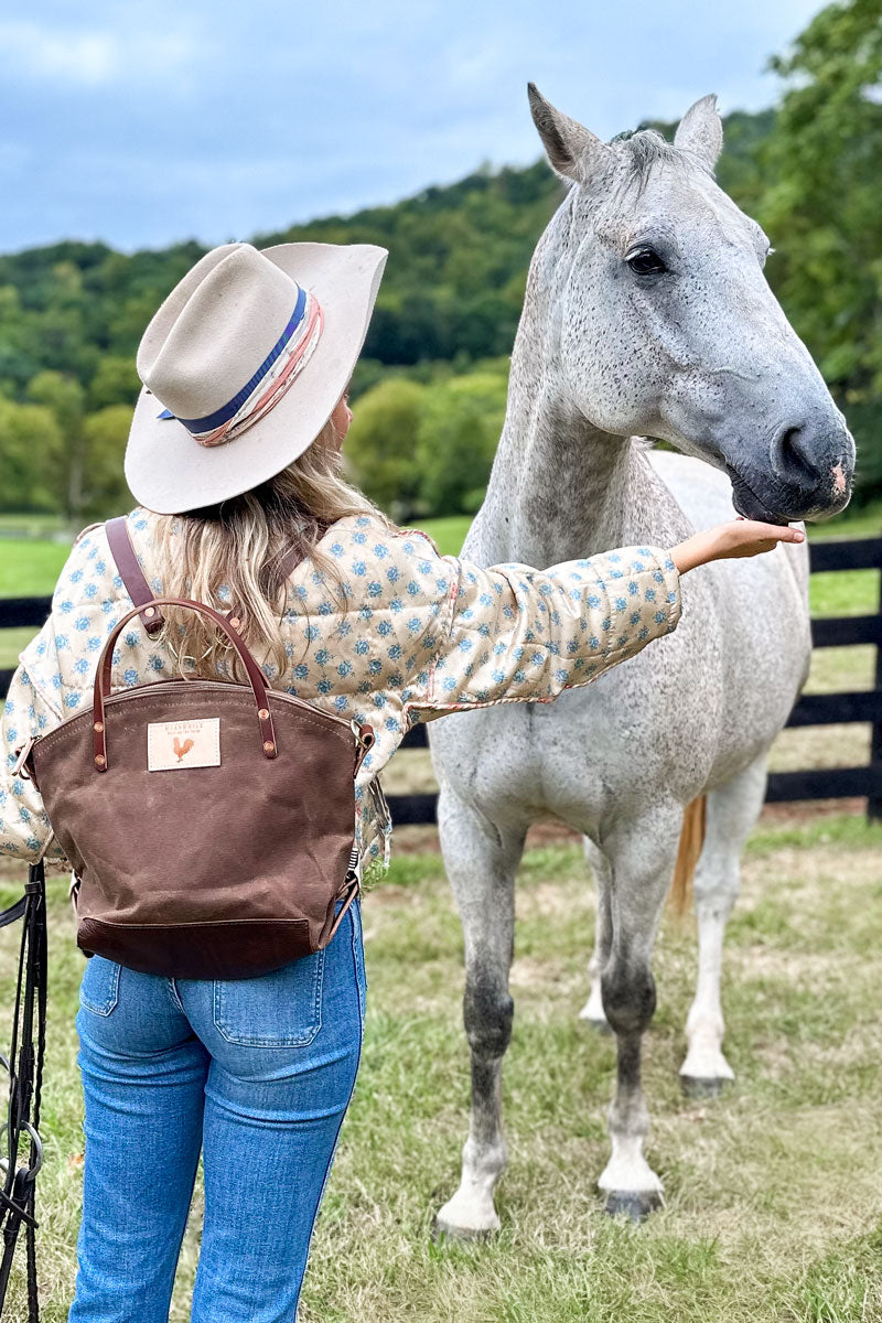 A woman wearing the field tan backpack with brown straps and the meanwhile logo.