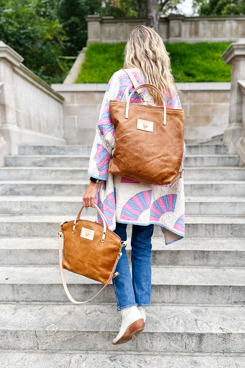 A woman wearing the camel brown backpack with tan straps and the meanwhile logo.