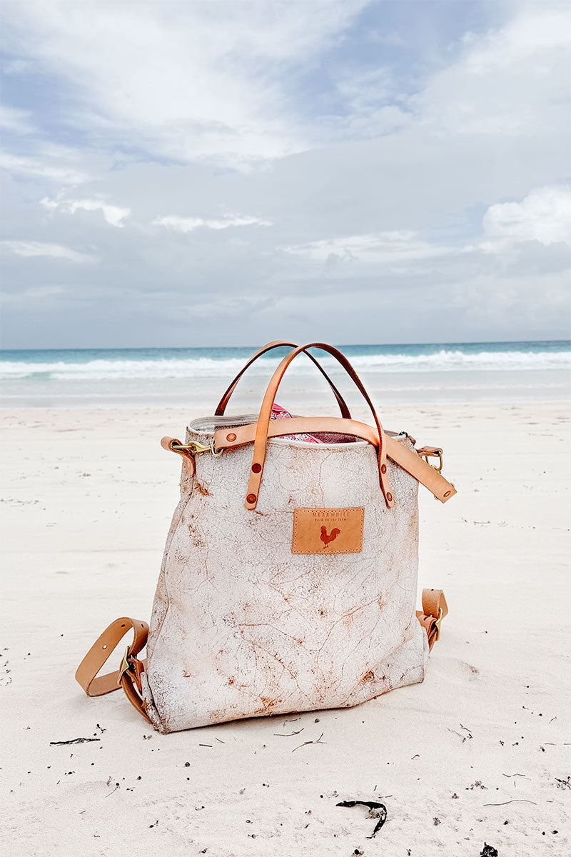 White birch leather convertible backpack sitting in the sand on a beach