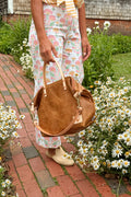 Person holding a brown leather bag in a garden setting
