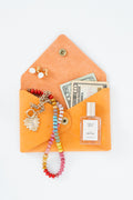 Orange leather Meanwhile Back on the Farm wallet with a colorful beaded necklace, earrings, and money