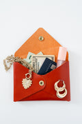 Red leather Meanwhile Back on the Farm wallet with money, a necklace, a card, and lip gloss