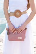 Person holding a pink leather bag with a blurred beach background