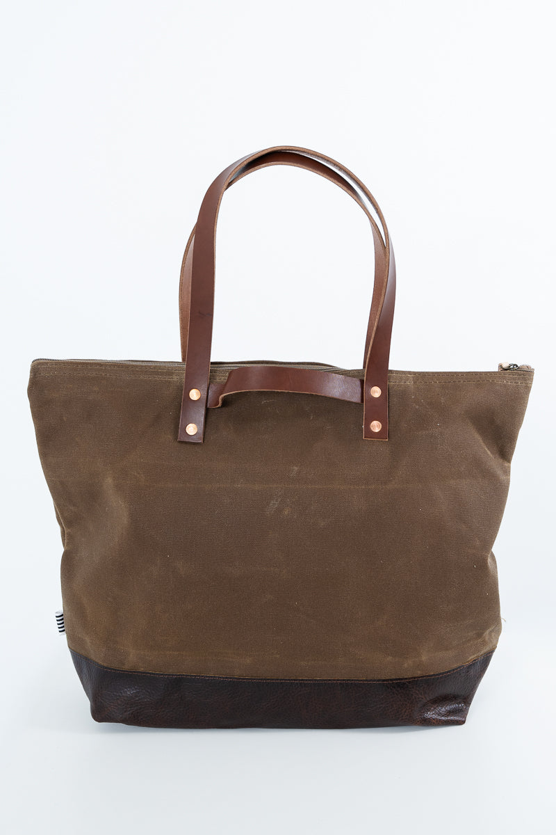 A brown canvas tote bag with dark brown leather handles and a dark brown leather base, photographed against a plain white background. Handmade by Meanwhile Back on the Farm in Lynchburg,VA