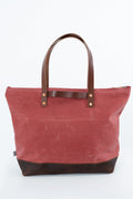 A red waxed canvas tote bag with dark brown leather handles and a matching dark brown leather base, shown against a plain white background. Handmade by Meanwhile Back on the Farm in Lynchburg,VA