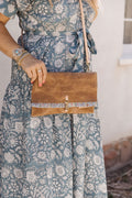 Woman wearing the camel brown bag with hook to close the bag, meanwhile logo, and a ruffle fabric along the edge of the opening of the bag.