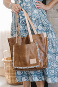 Woman holding the brown camel bag with the meanwhile logo and an outside pocket bordered with ruffles.