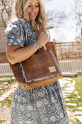 Woman outside holding the brown camel bag with the meanwhile logo and an outside pocket bordered with ruffles.
