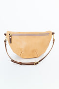 A light tan suede crescent-shaped belt bag with a brown leather strap and gold-tone hardware, shown against a plain white background.