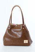 A brown leather handbag with dual shoulder straps, a floral patterned lining visible at the top, and a small beige brand patch on the lower right front.