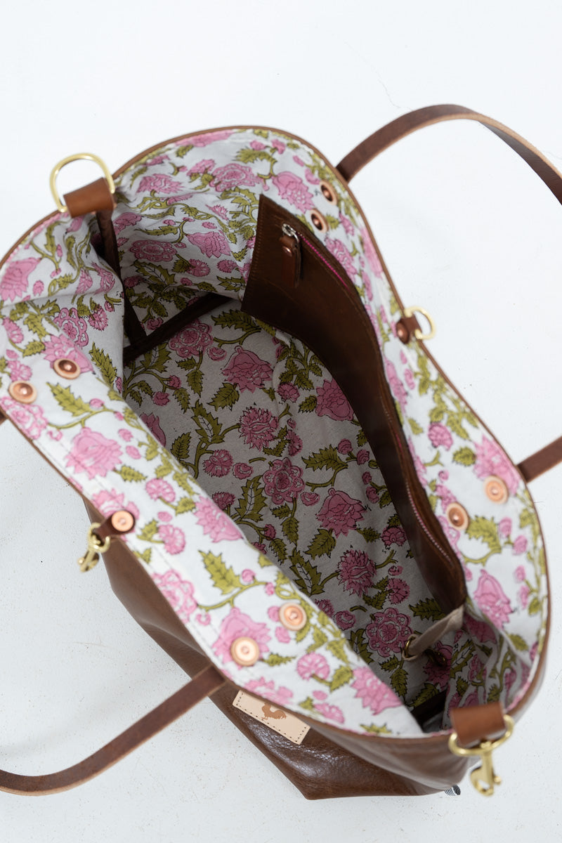 An overhead view of a brown leather handbag showing its floral-patterned interior lining with pink flowers and green leaves on a white background.