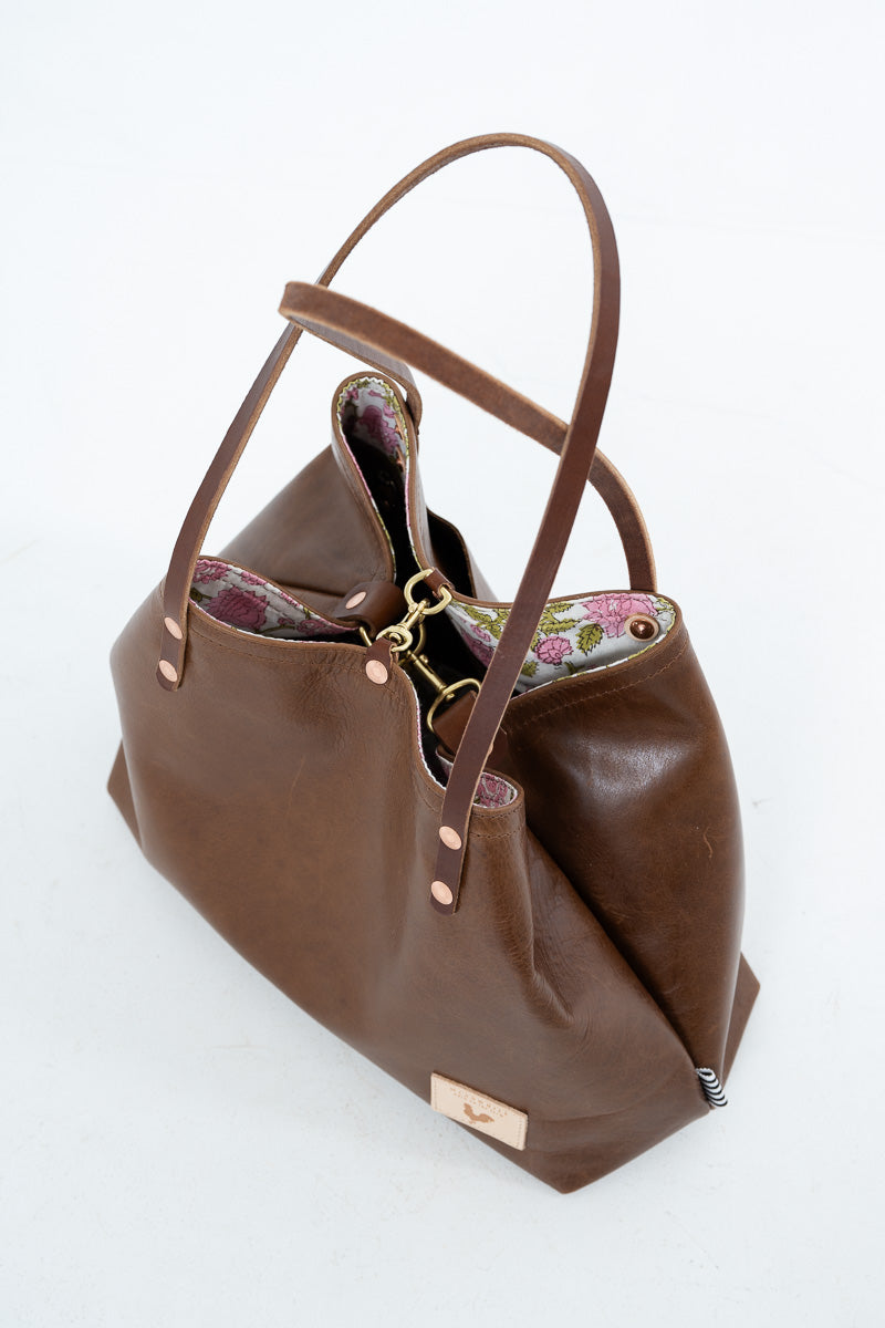 A brown leather shoulder bag with a floral patterned lining, gold-tone hardware, and a small metal logo plaque, photographed on a white background.