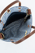 Close-up of the interior of a handbag with a blue and white floral patterned fabric lining, brown leather trim, and brass-tone hardware on a white background.