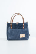 A navy blue textured leather tote bag with brown leather handles and a small beige brand patch on the front pocket, set against a clean white background.