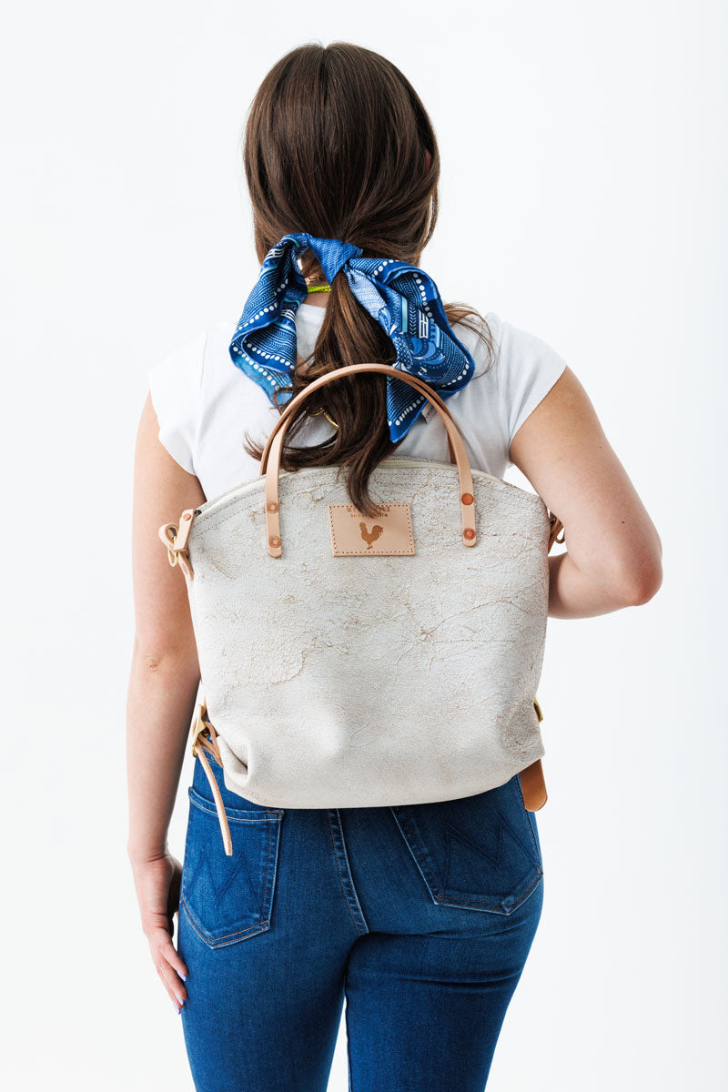 Woman wearing the birch white backpack with meanwhile logo and light brown straps.
