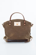 A brown canvas tote bag with dark brown leather trim, dual top handles, and a rectangular brand patch on the front, photographed against a plain white background. Handmade by Meanwhile Back on the Farm in Lynchburg,VA