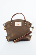 A brown waxed canvas tote bag with dark brown leather handles and a matching adjustable shoulder strap, featuring a beige brand patch with a rooster logo on the front. Handmade by Meanwhile Back on the Farm in Lynchburg,VA
