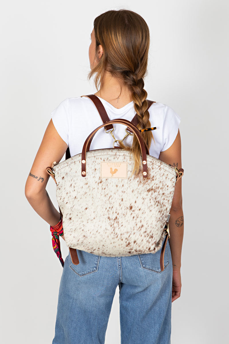 Woman wearing the hair on hide leather backpack with the meanwhile logo and brown straps.