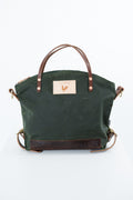 An olive green canvas tote bag with dark brown leather handles, trim, and base, featuring a tan leather brand patch with a rooster logo on the front. Handmade by Meanwhile Back on the Farm in Lynchburg,VA