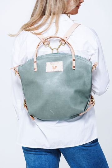 Model wearing sea foam green colored leather back pack style bag with cream colored straps.