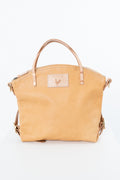 A light tan leather handbag with dual top handles and a small rectangular brand patch on the front, photographed against a plain white background. Handmade by Meanwhile Back on the Farm in Lynchburg,VA