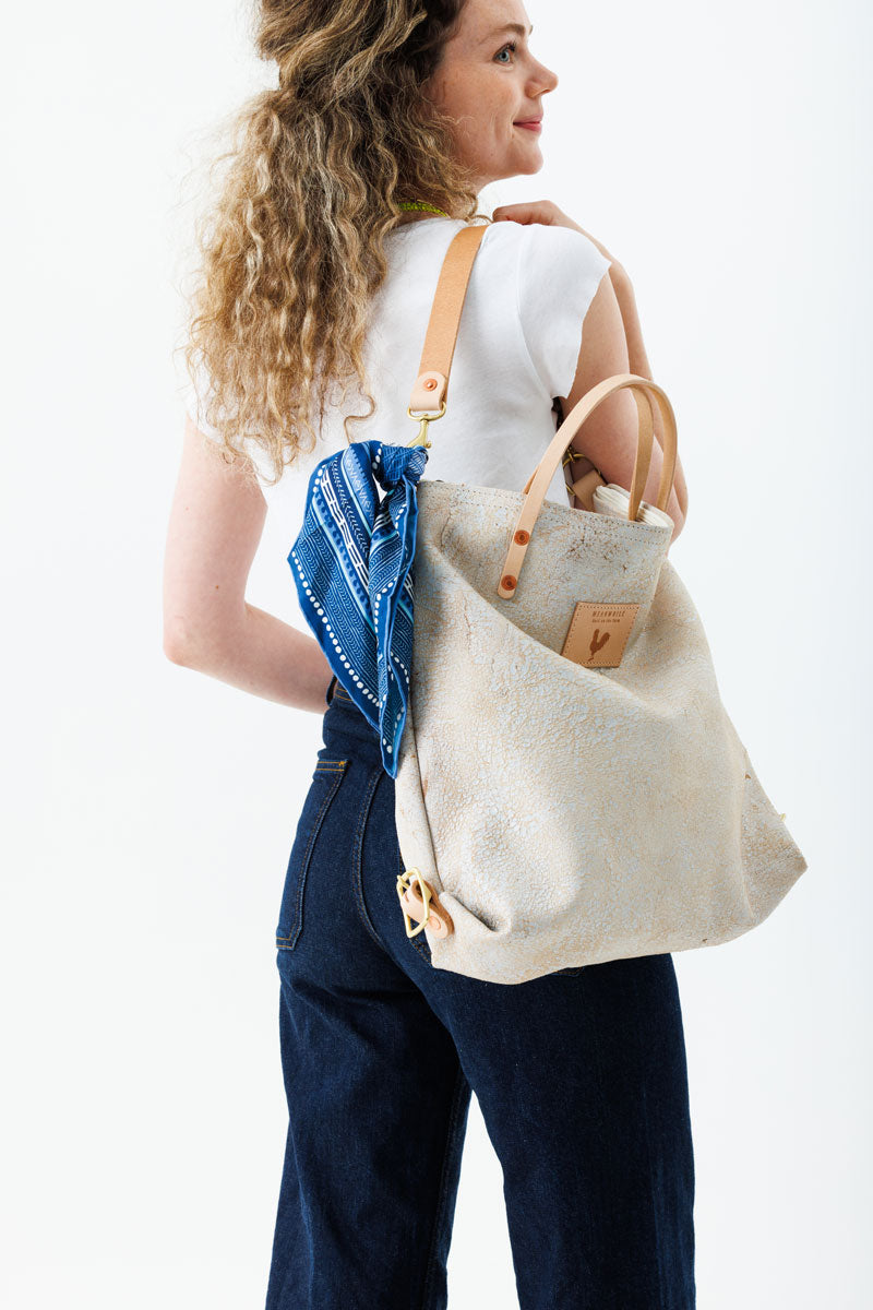 A woman holding the birch white bag with tan straps and the meanwhile logo decorated with a blue scarf.