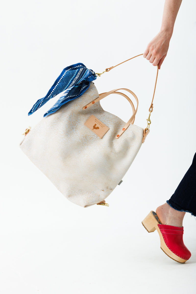 Woman swinging the birch white backpack with light brown straps, meanwhile logo, and a blue decorative scarf.