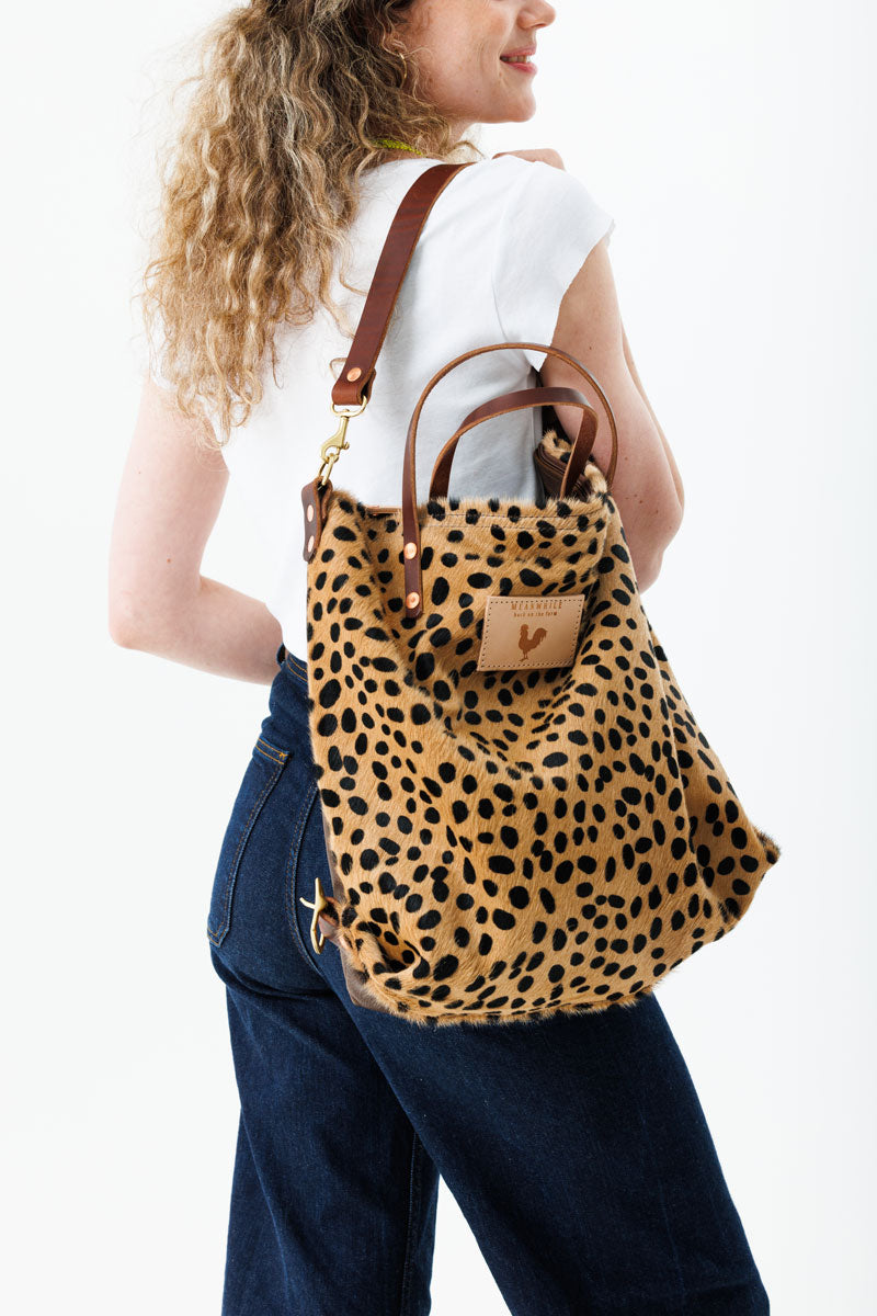 Woman holding cheetah print bag with meanwhile logo and has a cross body strap.