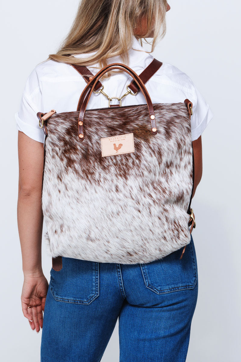 Model wearing brushed brown cowhide backpack style bag with brown leather straps.