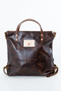 A dark brown distressed leather handbag with double top handles, a front leather patch featuring a rooster logo, and brass-tone hardware, photographed against a plain white background. Handmade by Meanwhile Back on the Farm in Lynchburg,VA