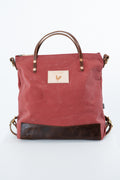 A red canvas tote bag with dark brown leather handles, a bottom panel, and hardware, featuring a small beige patch with a rooster logo on the front. Handmade by Meanwhile Back on the Farm in Lynchburg,VA