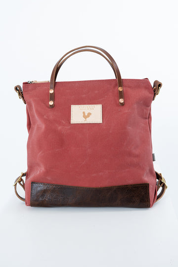 A red canvas tote bag with dark brown leather handles, a bottom panel, and hardware, featuring a small beige patch with a rooster logo on the front. Handmade by Meanwhile Back on the Farm in Lynchburg,VA