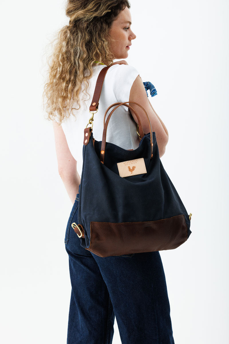A woman wearing the navy backpack with dark brown straps and the meanwhile logo.