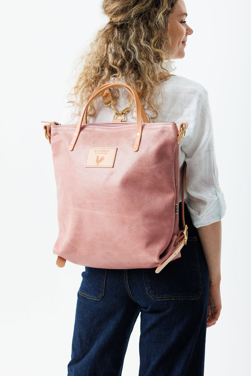 Model wearing large rose colored leather back pack style bag with pink straps.