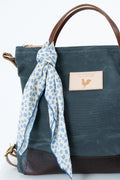 A dark teal canvas tote bag with brown leather handles and bottom trim, featuring a cream leather patch with a rooster logo and a blue-and-white floral scarf tied around the handle. Handmade by Meanwhile Back on the Farm in Lynchburg,VA