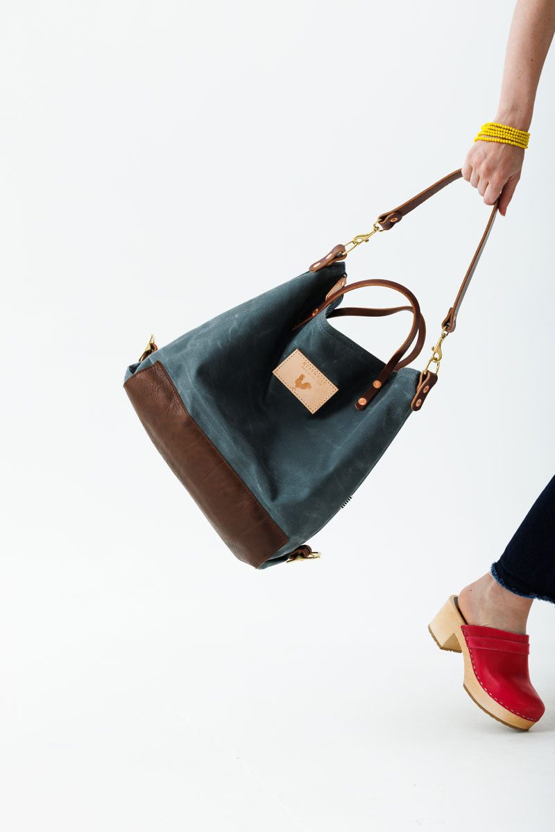 A woman wearing the slate grey bag with mocha brown straps and the meanwhile logo.