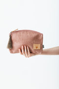 A hand holding a rose colored makeup bag with a tassel zipper.  