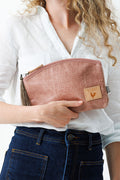 A woman holding a rose colored makeup bag with a tassel zipper.  