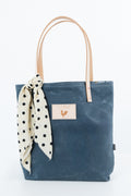 A large slate blue tote bag with tan leather handles. Handles have a white polka dot scarf tied to it. Handmade by Meanwhile Back on the Farm in Lynchburg,VA