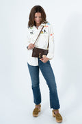 A woman modeling a white long-sleeve button-up shirt with colorful embroidered details, paired with blue jeans, brown suede platform shoes, and a brown crossbody bag, set against a plain white studio background. Handmade by Meanwhile Back on the Farm in Lynchburg,VA