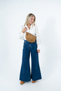 A woman modeling a white long-sleeve blouse, dark blue wide-leg denim pants, and a tan brown suede crossbody bag against a plain white studio background. Handmade by Meanwhile Back on the Farm in Lynchburg,VA