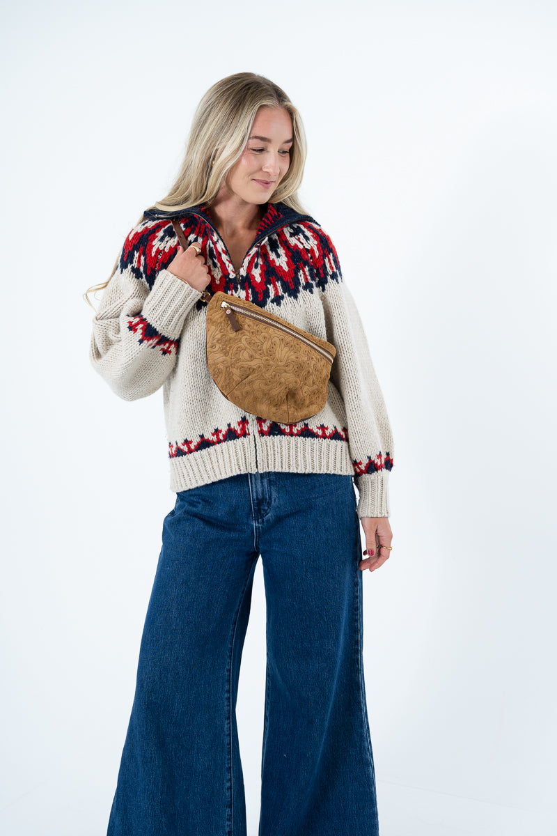 A woman wearing a cream knit zip-up sweater with a red and navy Fair Isle pattern, blue wide-leg jeans, and a brown suede crossbody bag, photographed against a plain white studio background. Handmade by Meanwhile Back on the Farm in Lynchburg,VA
